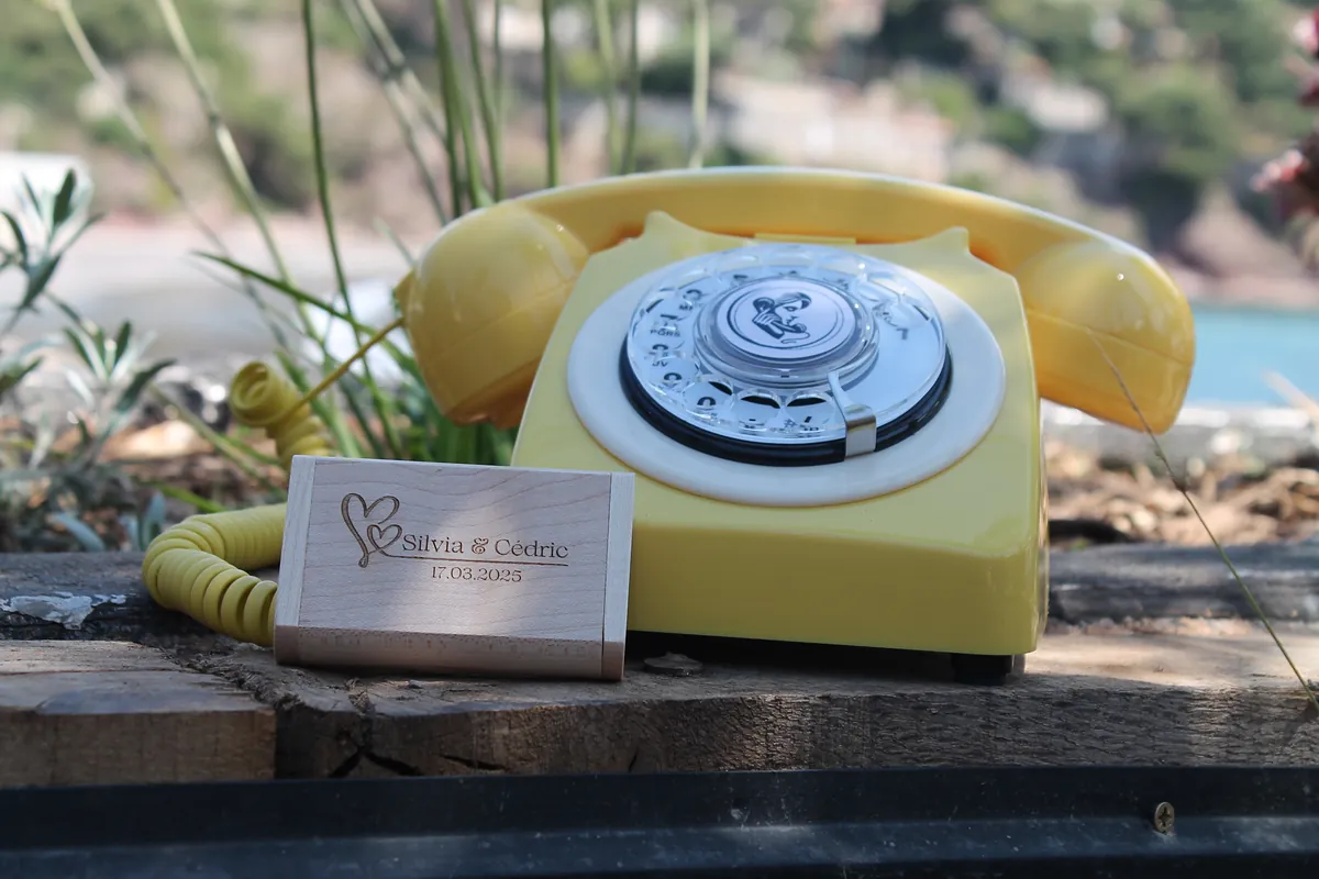 Wooden USB stick engraved with names and date, in front of a yellow vintage phone
