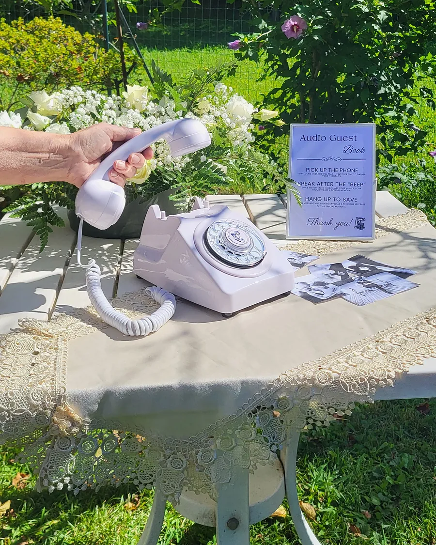 Téléphone vintage blanc et cadre du livre d’or audio sur une petite table dans un jardin