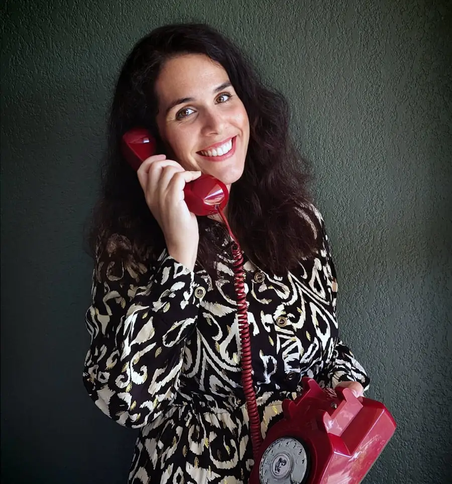 Femme souriant tenant un téléphone rétro rouge pour le livre d'or audio.